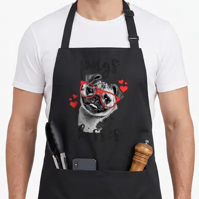 Pug valentine's day apron - Cartoon pug in red glasses with pugs and kisses text and red hearts — shown on a black cotton canvas apron against a white background