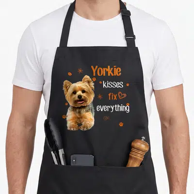 Kiss yorkshire apron - Cartoon Yorkie with orange paw prints and text reading kisses fix everything — shown on a black cotton canvas apron against a white background