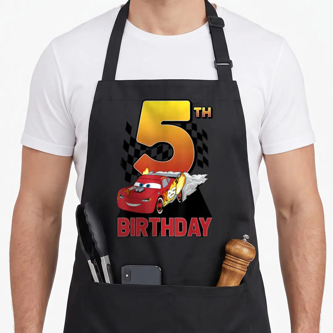 Peel car apron - Red race car with fire and smoke in front of number 5 and checkered flag with BIRTHDAY text — shown on a black cotton canvas apron against a white background