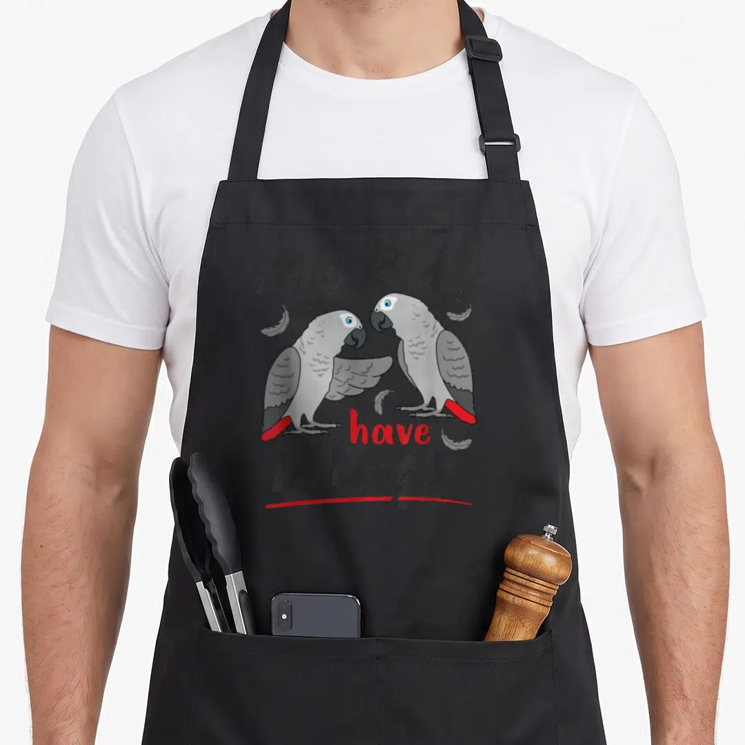 Wing bird apron - Two grey parrots facing each other with red tail feathers and My Kids Have Wings text — shown on a black cotton canvas apron against a white background