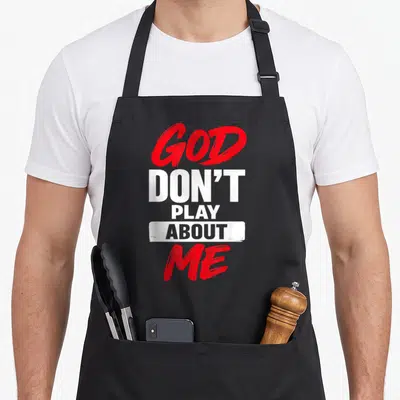 Play jesus christian apron - Stacked red and white text reading GOD DON'T PLAY ABOUT ME on grey background — shown on a black cotton canvas apron against a white background