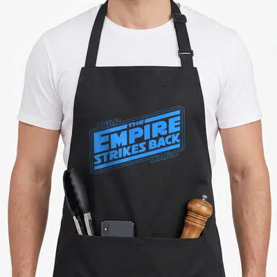 Empire logo officially apron - Blue stacked text reading Star Wars The Empire Strikes Back inside a rectangular frame — shown on a black cotton canvas apron against a white background