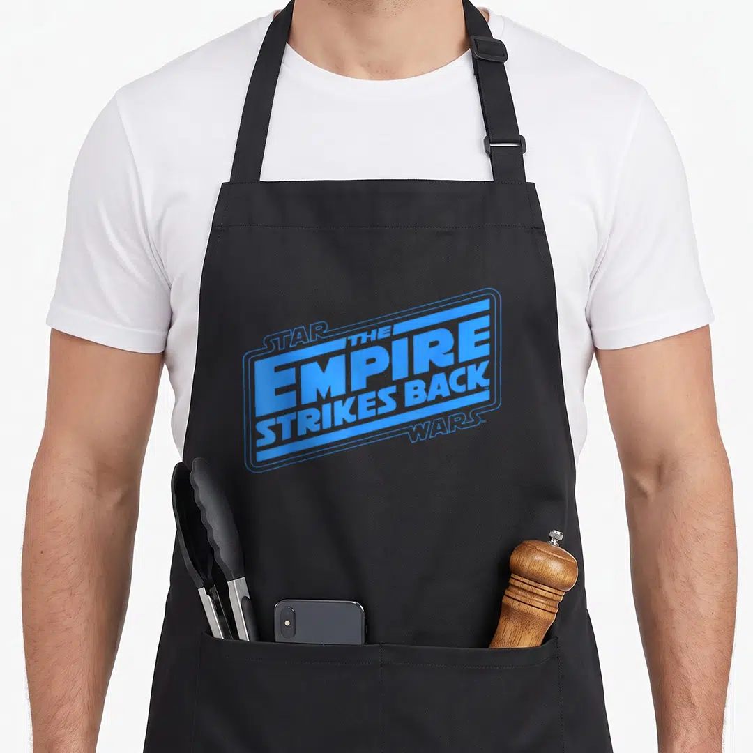 Empire logo officially apron - Blue stacked text reading Star Wars The Empire Strikes Back inside a rectangular frame — shown on a black cotton canvas apron against a white background