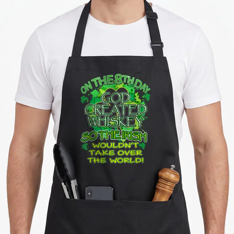 Created funny irish aprons - Green white and yellow text saying On The 8th Day God Created Whiskey So The Irish — shown on a black cotton canvas apron against a white background
