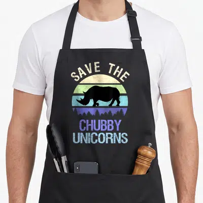 Sunset unicorn apron - Black rhino silhouette in front of striped beige green blue purple sun with SAVE THE CHUBBY — shown on a black cotton canvas apron against a white background