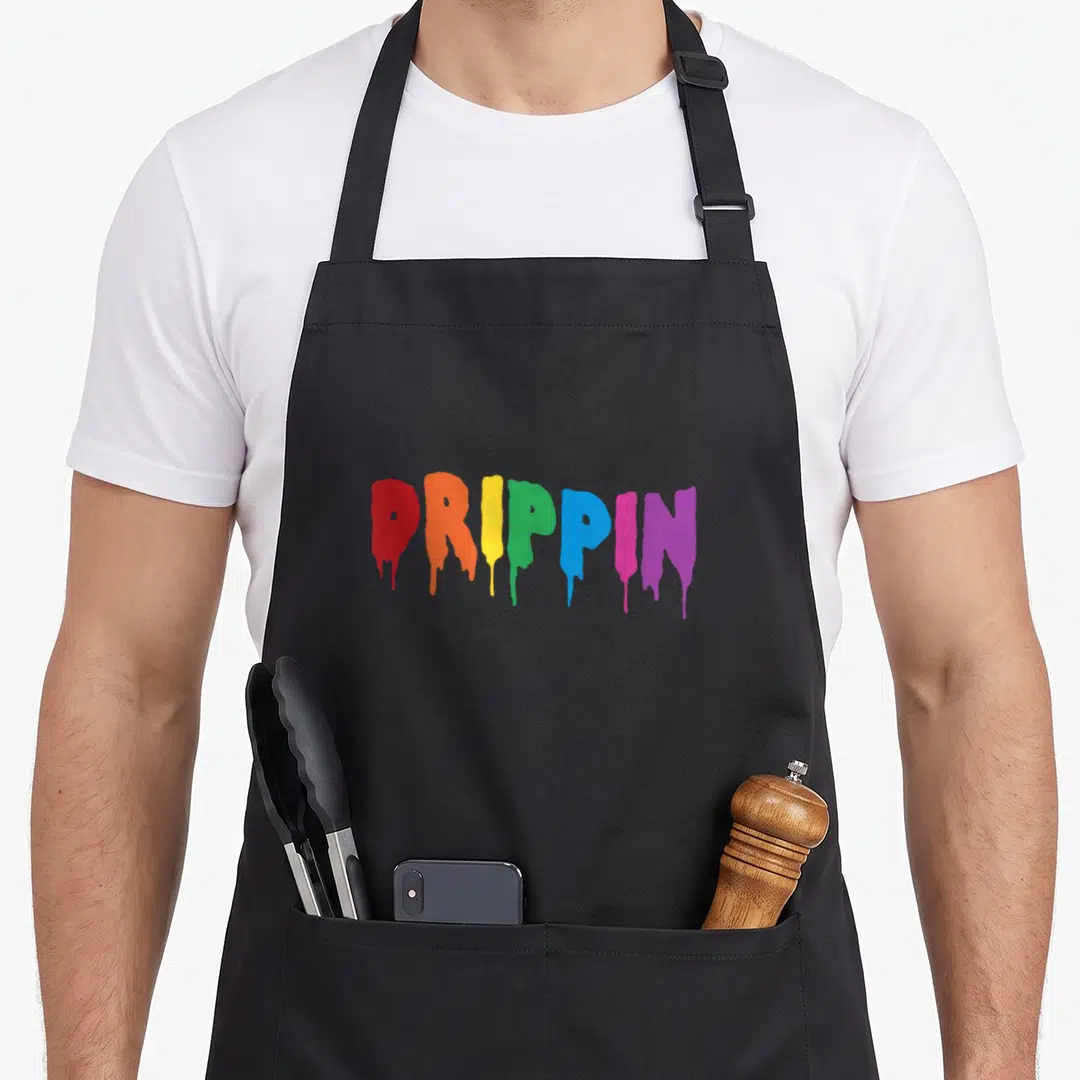 Drippin colorful aprons - Rainbow dripping text reading DRIPPIN in red orange yellow green blue purple — shown on a black cotton canvas apron against a white background