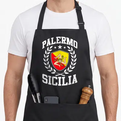 Trinacria sicily apron - Retro shield with PALERMO SICILIA text, red yellow figure, three stars, and laurel wreath — shown on a black cotton canvas apron against a white background