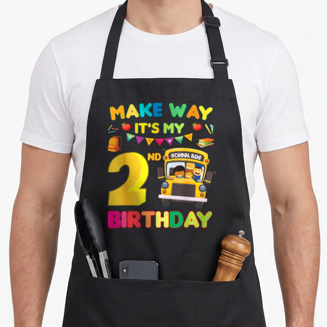 Way 2nd apron - School bus, number 2, rainbow text, school supplies, bunting, yellow red blue green — shown on a black cotton canvas apron against a white background