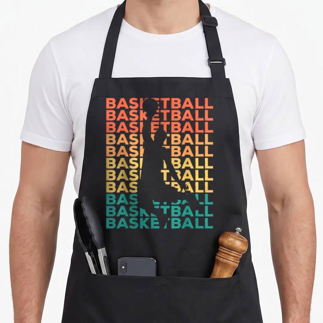 Cute basketball player apron - Grey basketball player silhouette over stacked red orange yellow and teal BASKETBALL text — shown on a black cotton canvas apron against a white background