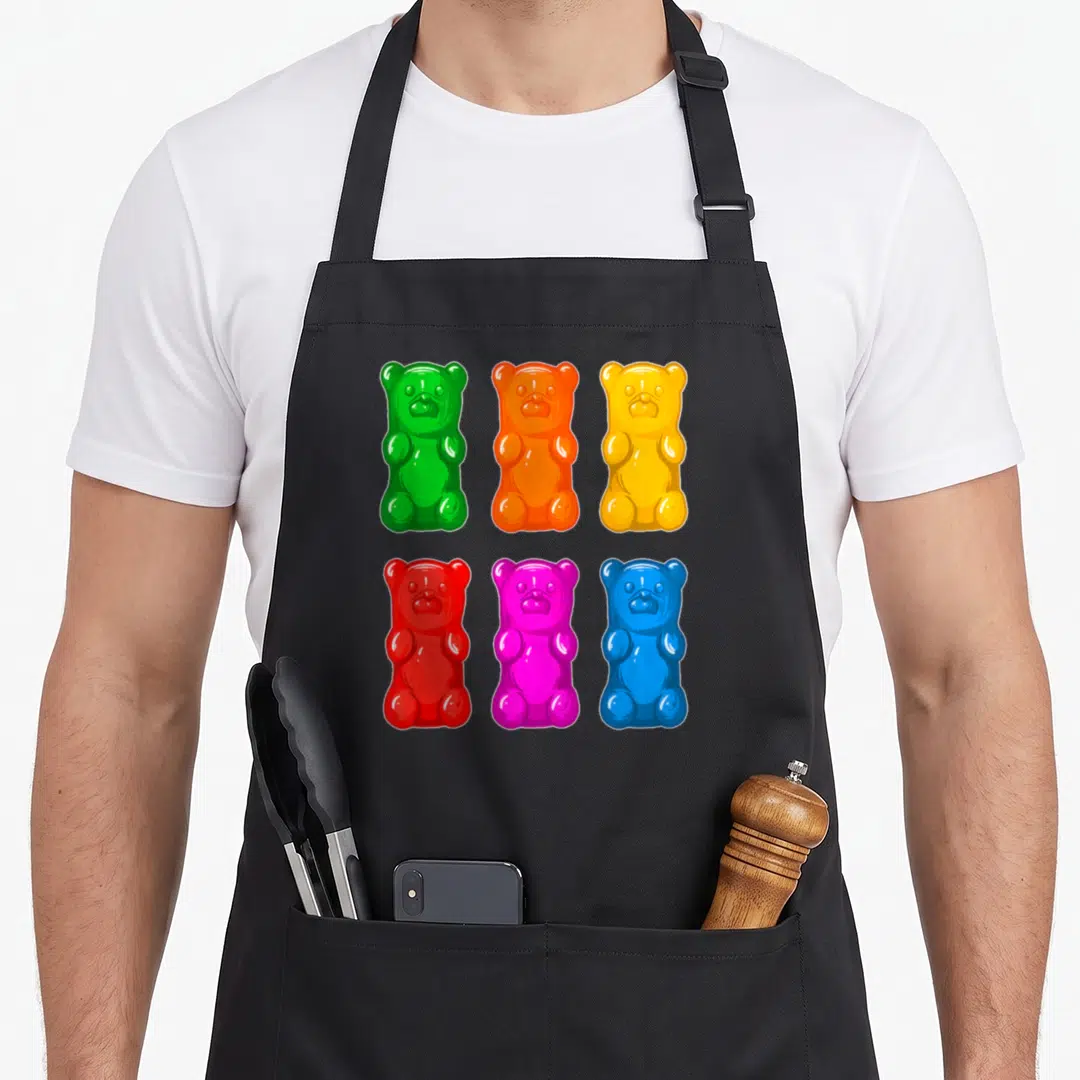 Youth bear apron - Six cartoon gummy bears in green, orange, yellow, red, pink, and blue arranged in two rows — shown on a black cotton canvas apron against a white background