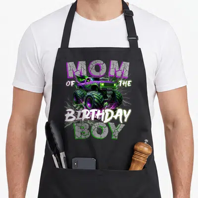 Monster family truck apron - Purple and green monster truck with lightning and MOM OF THE BIRTHDAY BOY text — shown on a black cotton canvas apron against a white background