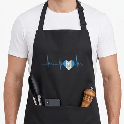 Heartbeat guatemalan aprons - Blue EKG pulse line with a heart shape containing vertical blue white and green flag — shown on a black cotton canvas apron against a white background