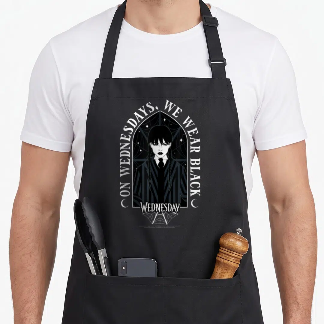 Wednesday goth apron - On Wednesdays We Wear Black text over gothic arch with woman portrait and spiderweb — shown on a black cotton canvas apron against a white background