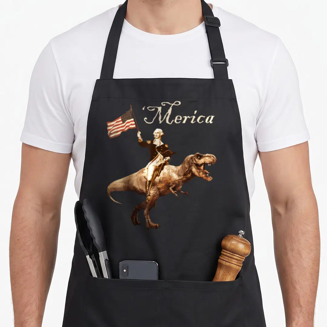 George t-rex apron - George Washington riding a brown T-Rex holding a flag with ‘Merica text in cream script — shown on a black cotton canvas apron against a white background