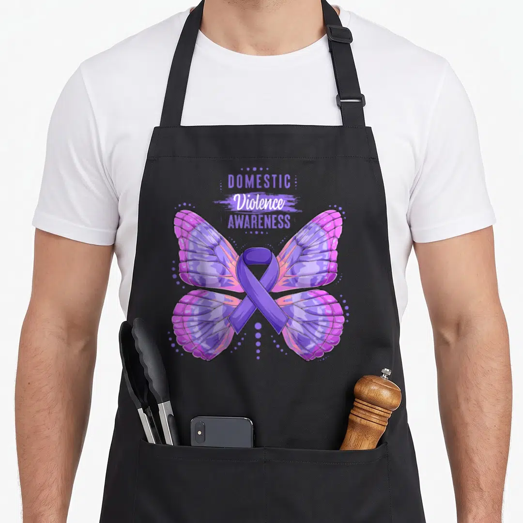 Butterfly domestic aprons - Stacked text above purple butterfly with ribbon body and surrounding dots — shown on a black cotton canvas apron against a white background