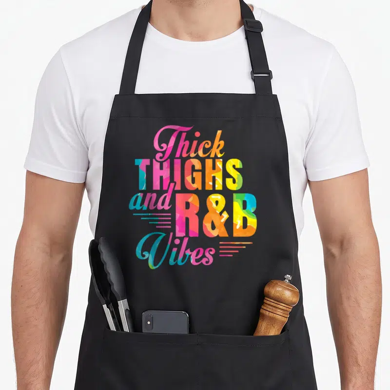 Thick r aprons - Stacked multicolor typography reading Thick THIGHS and R&B Vibes with horizontal accent lines — shown on a black cotton canvas apron against a white background