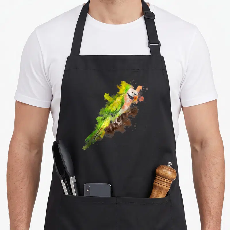 Watercolor parakeet dad apron - Green and yellow watercolor parrot perched on a brown branch with paint splatters — shown on a black cotton canvas apron against a white background