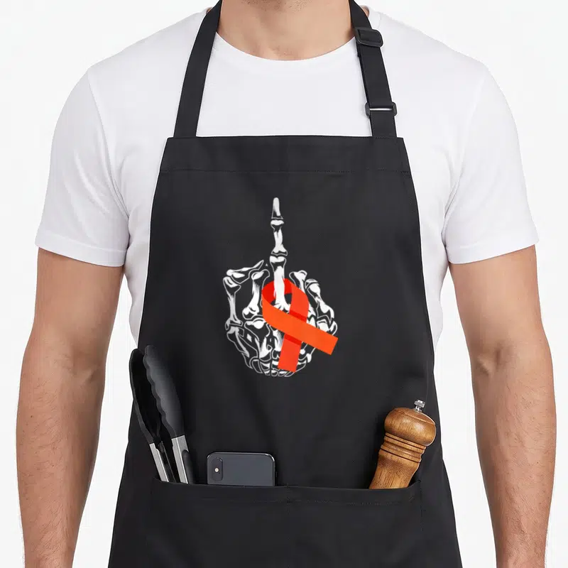 Leukemia cancer awareness apron - White skeleton hand middle finger gesture wrapped in red awareness ribbon line art — shown on a black cotton canvas apron against a white background