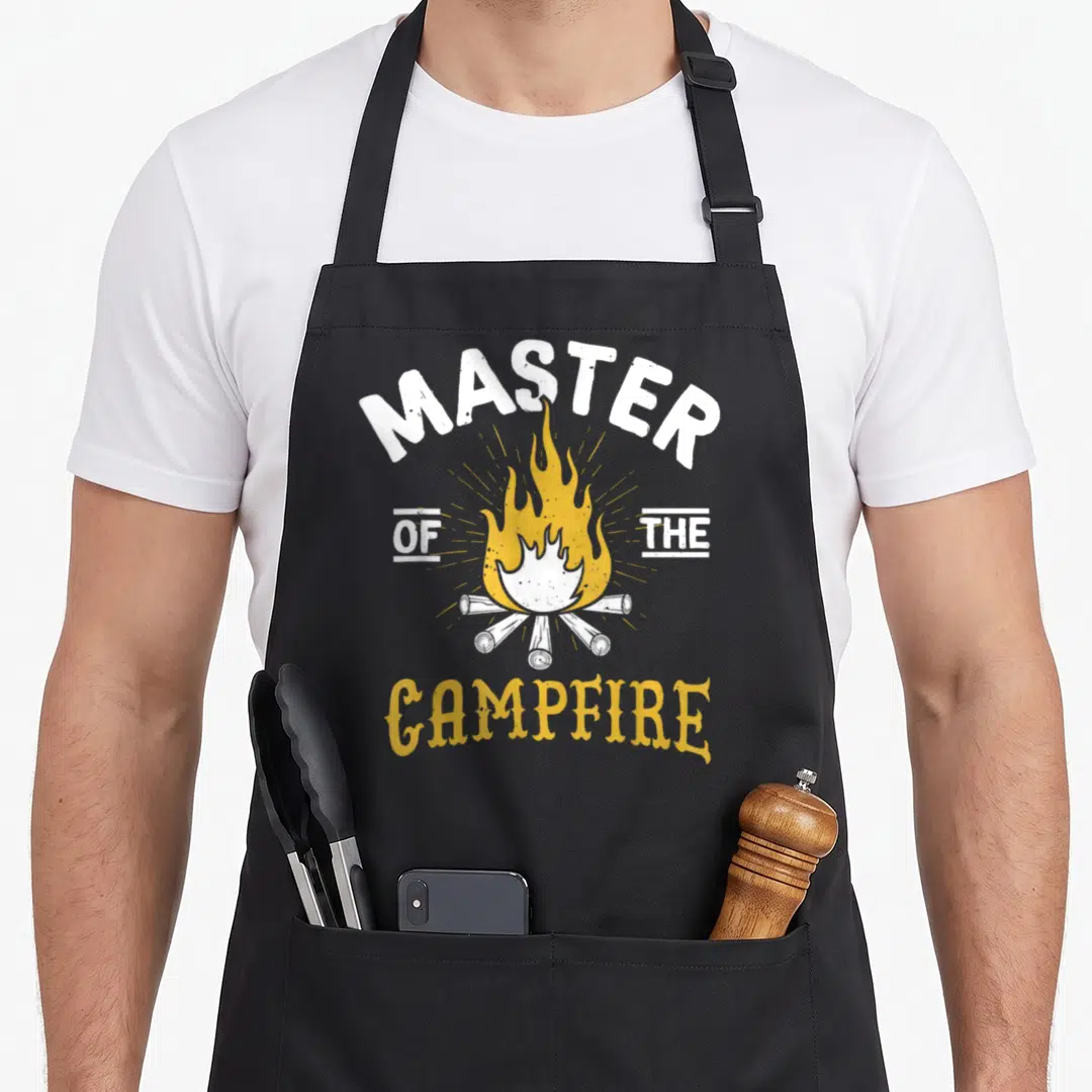 Campfire outdoor apron - White and yellow distressed campfire graphic with arched MASTER OF THE CAMPFIRE text — shown on a black cotton canvas apron against a white background