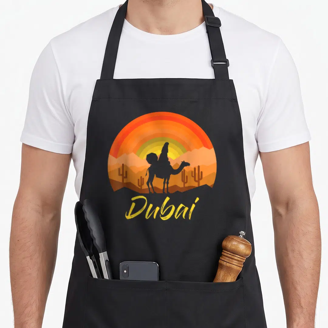 Arab dubai apron - Camel silhouette against orange sunset with cacti and yellow Dubai text — shown on a black cotton canvas apron against a white background