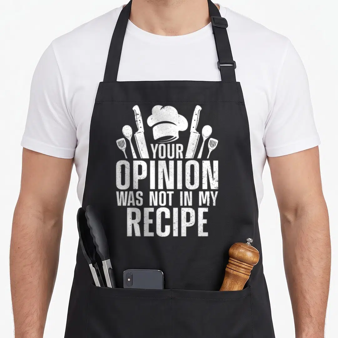 Vintage culinary aprons - White chef hat and utensils above text Your Opinion Was Not In My Recipe distressed style — shown on a black cotton canvas apron against a white background