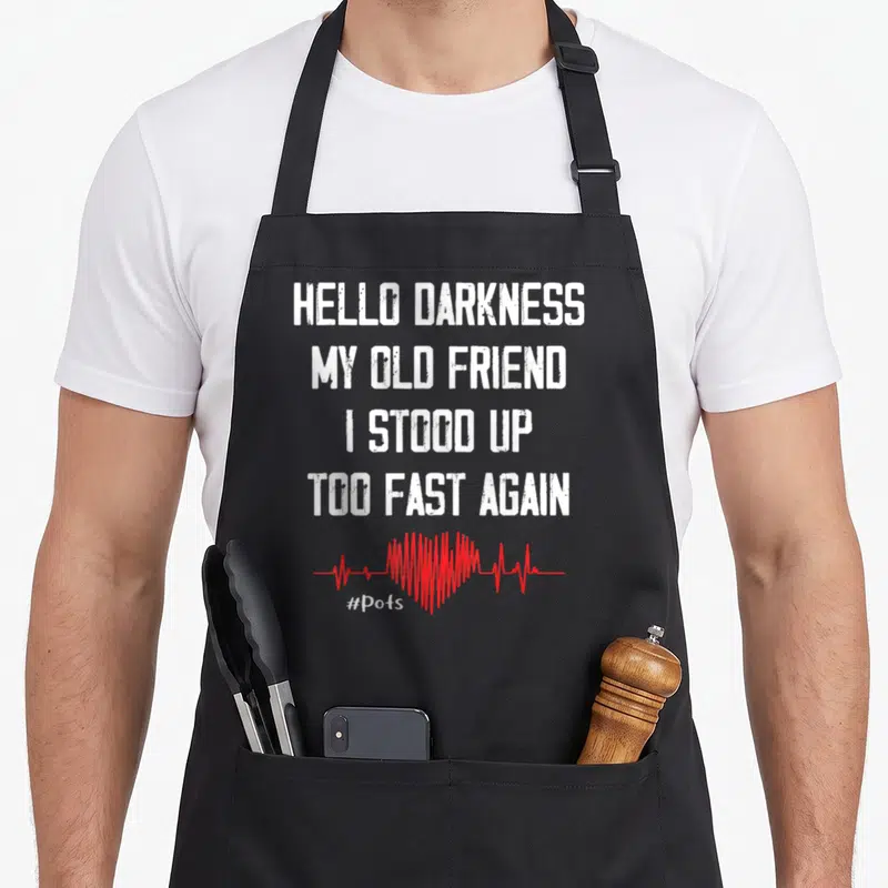 Stood friends apron - White stacked text Hello Darkness My Old Friend I Stood Up Too Fast Again above red heartbeat — shown on a black cotton canvas apron against a white background