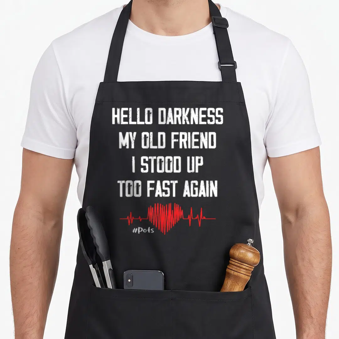 Stood friends apron - White stacked text Hello Darkness My Old Friend I Stood Up Too Fast Again above red heartbeat — shown on a black cotton canvas apron against a white background