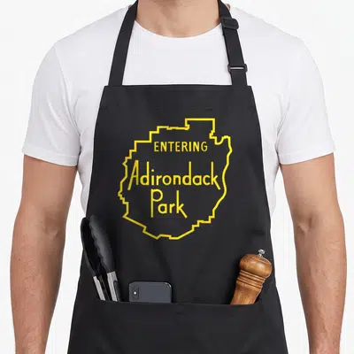 Entering adirondacks apron - Yellow Adirondack Park map outline with centered entering text — shown on a black cotton canvas apron against a white background