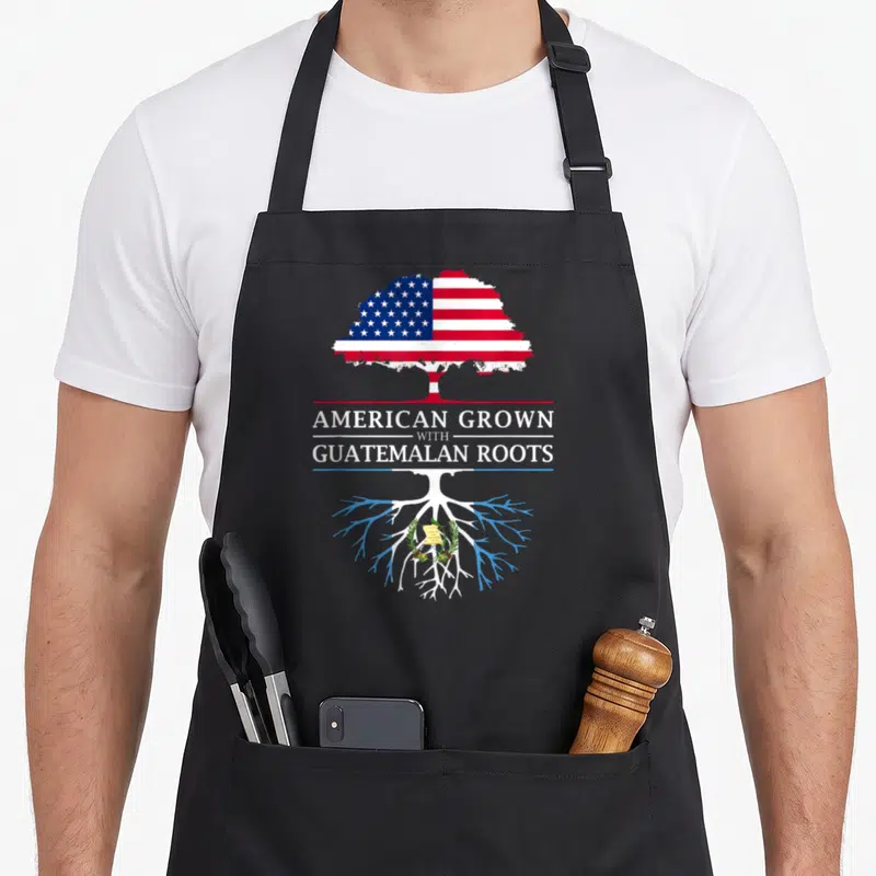 Grown guatemalan aprons - Tree with US flag canopy and Guatemala roots containing coat of arms and stacked white text — shown on a black cotton canvas apron against a white background