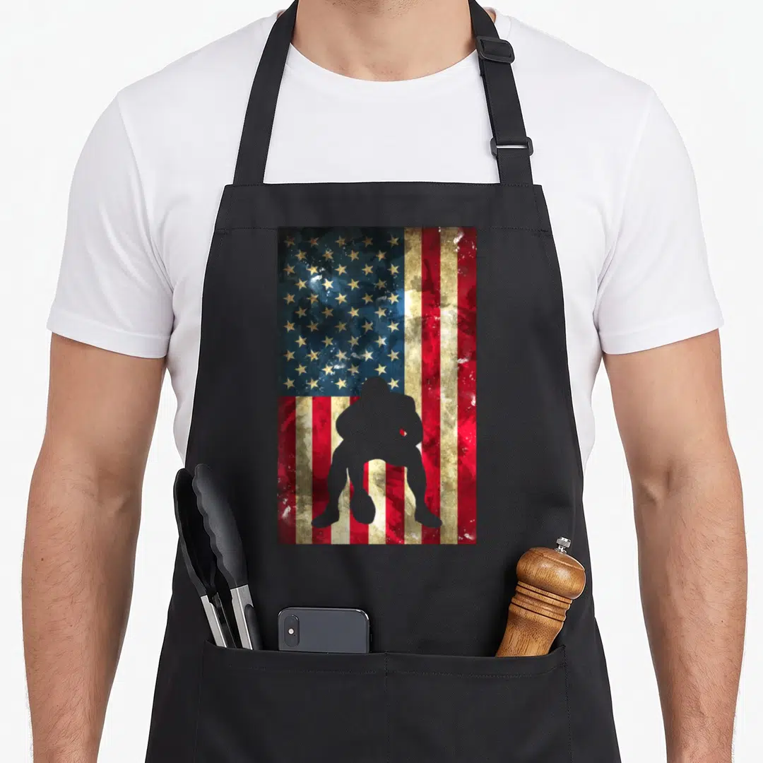 Football american flag apron - Distressed US flag with grey crouching football player silhouette, no text — shown on a black cotton canvas apron against a white background