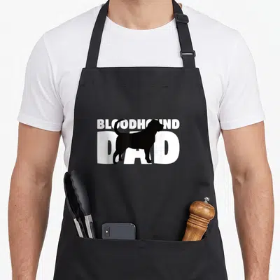 Bloodhound father dog apron - Black bloodhound silhouette overlapping white text reading BLOODHOUND DAD — shown on a black cotton canvas apron against a white background