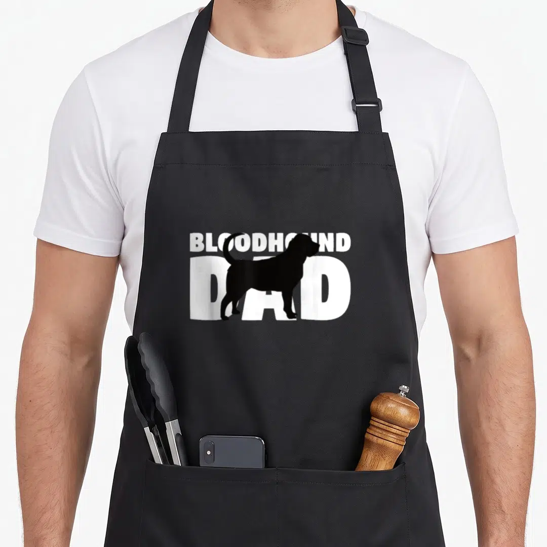 Bloodhound father dog apron - Black bloodhound silhouette overlapping white text reading BLOODHOUND DAD — shown on a black cotton canvas apron against a white background