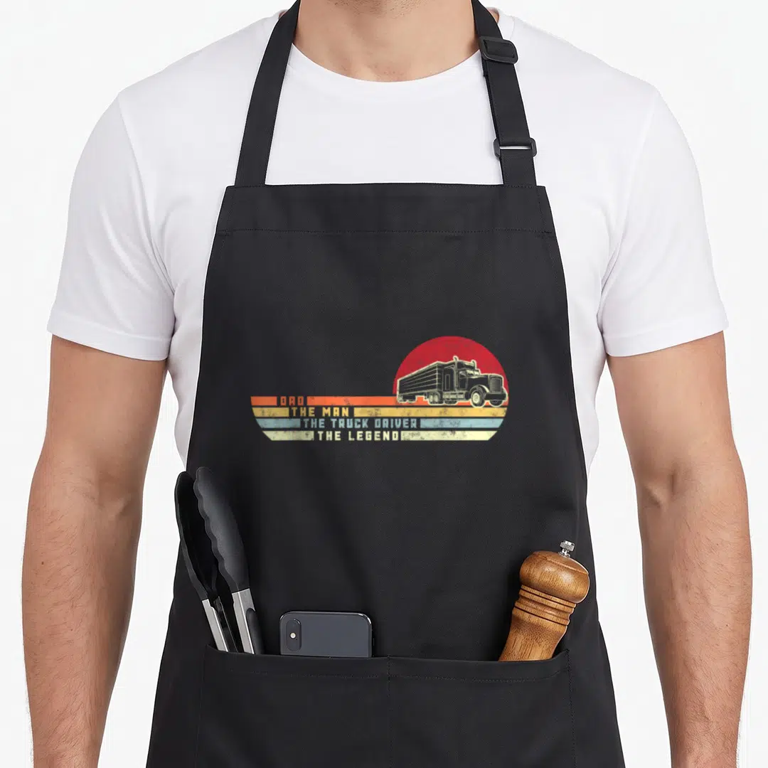 Legend semi truck apron - Retro truck graphic with four colored stripes reading Dad The Man Truck Driver Legend — shown on a black cotton canvas apron against a white background