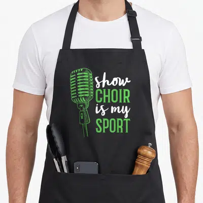 Show chorus apron - Green microphone graphic next to stacked white and green text reading show choir is my sport — shown on a black cotton canvas apron against a white background