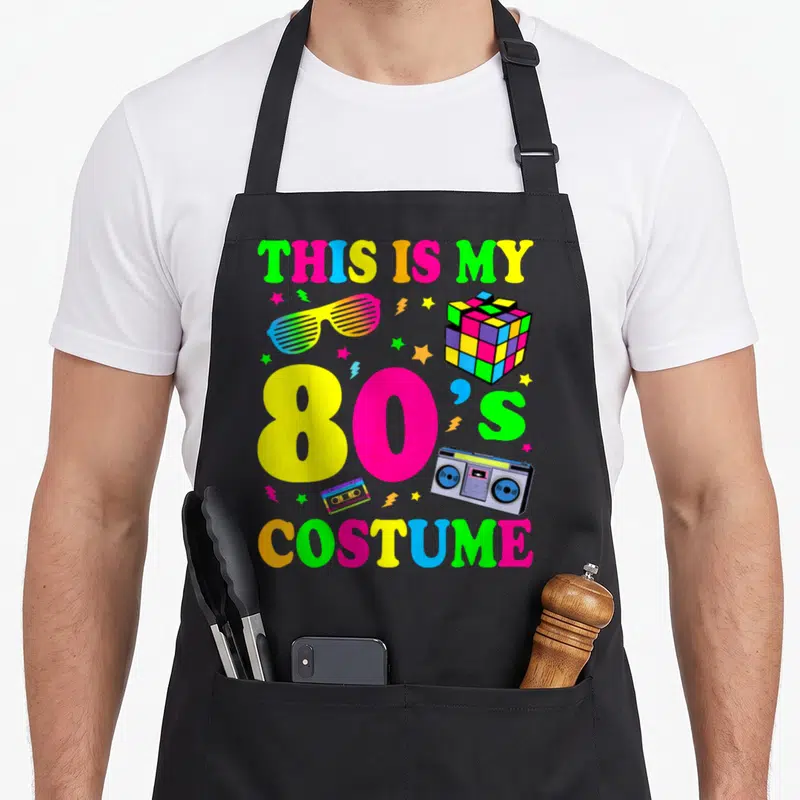 80s cute halloween aprons - THIS IS MY 80'S COSTUME text with boombox and Rubik's cube in neon colors — shown on a black cotton canvas apron against a white background