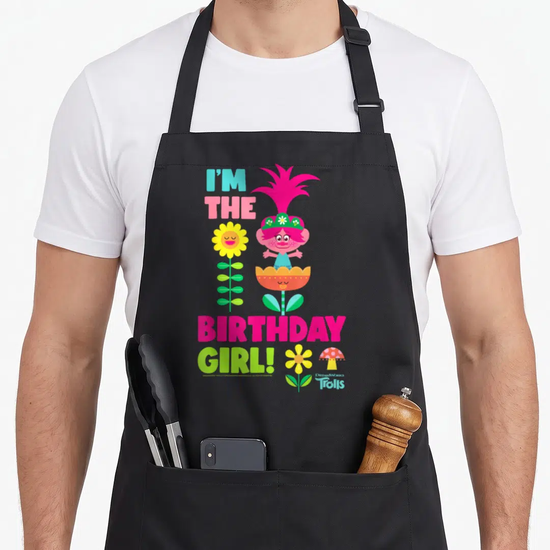 Troll birthday apron - Pink troll character with tall flower and mushroom, I'M THE BIRTHDAY GIRL! text in bright colors — shown on a black cotton canvas apron against a white background