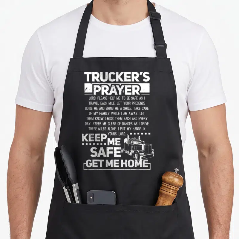 Trucker safe apron - White distressed truck illustration beside Trucker's Prayer text and Keep Me Safe Get Me Home — shown on a black cotton canvas apron against a white background