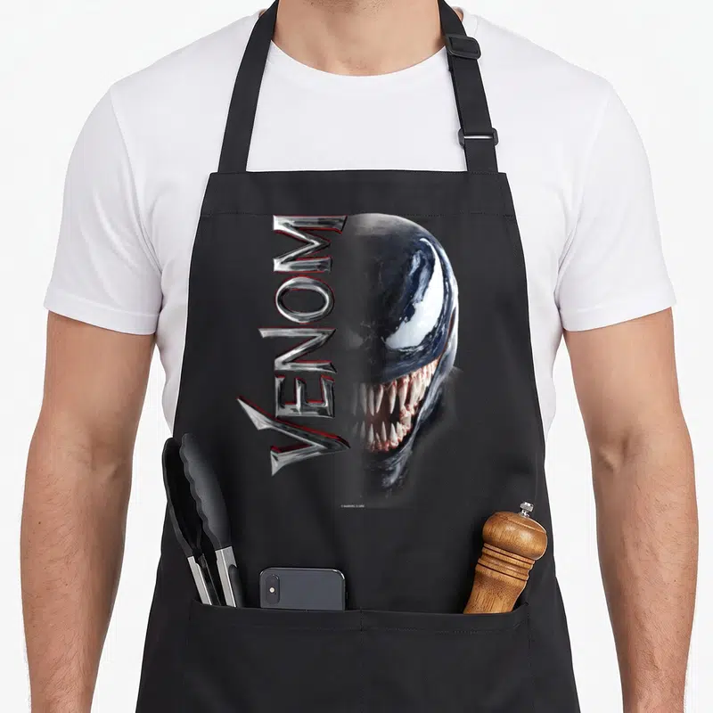 Middle split apron - Vertical Venom text overlapping a realistic character face in black silver white and red — shown on a black cotton canvas apron against a white background