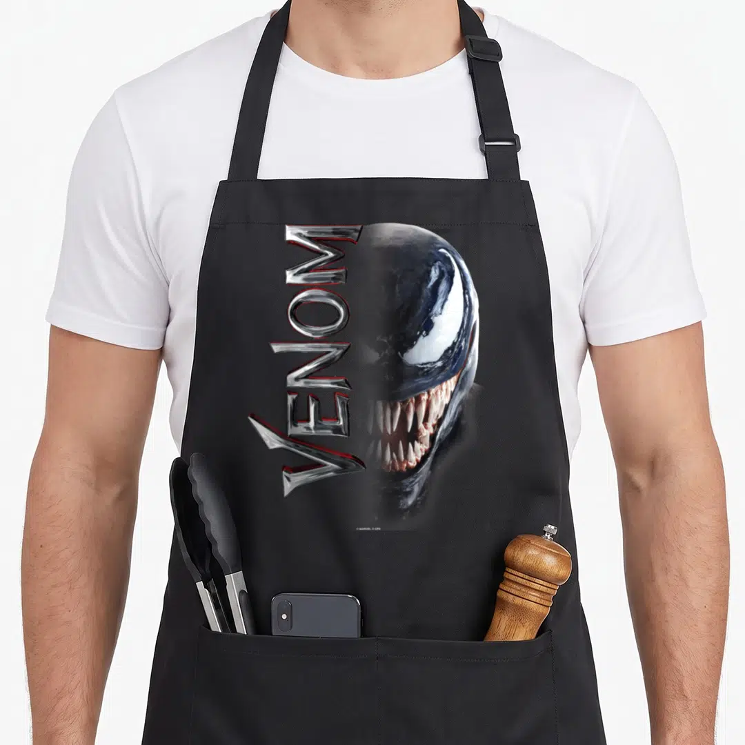 Middle split apron - Vertical Venom text overlapping a realistic character face in black silver white and red — shown on a black cotton canvas apron against a white background