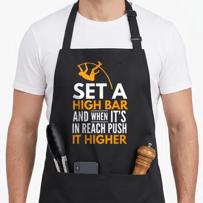Pole vault track apron - Gymnast silhouette above stacked white and orange text reading SET A HIGH BAR AND WHEN IT'S — shown on a black cotton canvas apron against a white background