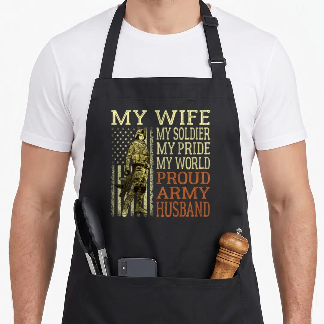 Hero husband wife aprons - Female soldier in camo holding rifle beside stacked beige and orange text reading My Wife My — shown on a black cotton canvas apron against a white background