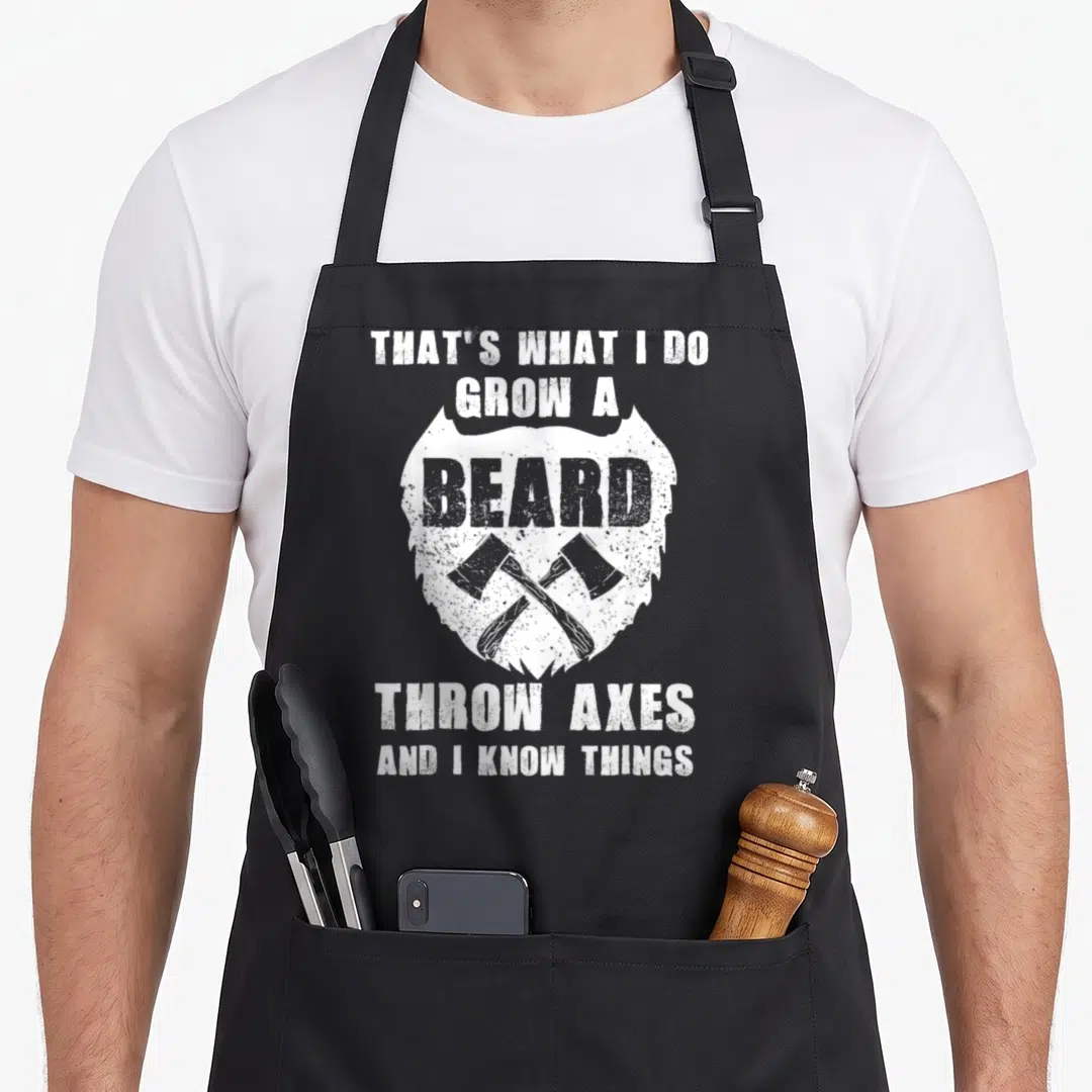Throw beard apron - Distressed white text above and below a beard shape containing two crossed axes — shown on a black cotton canvas apron against a white background