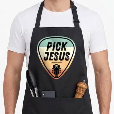 Pick jesus music christian apron - Guitar pick shape with teal orange cream stripes and PICK JESUS text — shown on a black cotton canvas apron against a white background