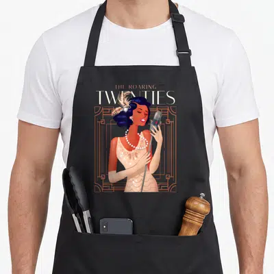 Roaring 1920s apron - Singing woman with microphone and feather headpiece in orange art deco frame with THE ROARING — shown on a black cotton canvas apron against a white background