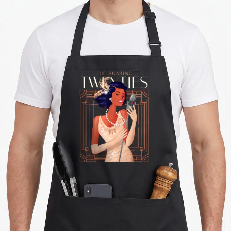 Roaring 1920s apron - Singing woman with microphone and feather headpiece in orange art deco frame with THE ROARING — shown on a black cotton canvas apron against a white background