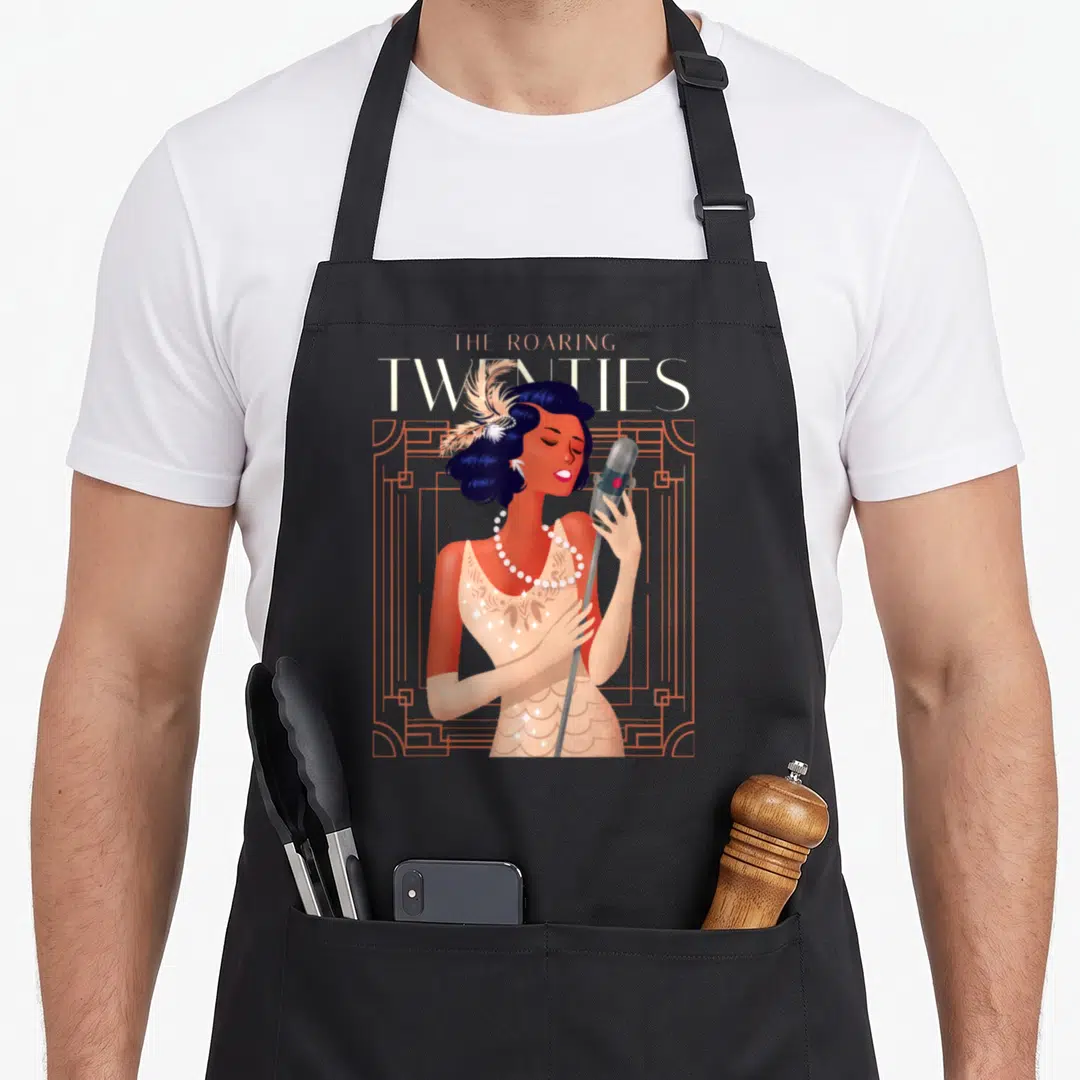 Roaring 1920s apron - Singing woman with microphone and feather headpiece in orange art deco frame with THE ROARING — shown on a black cotton canvas apron against a white background