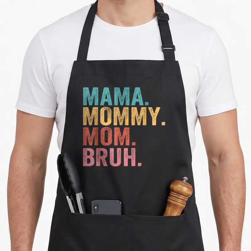 Bruh mother's day aprons - Stacked text MAMA MOMMY MOM BRUH in teal yellow red and pink vintage font — shown on a black cotton canvas apron against a white background