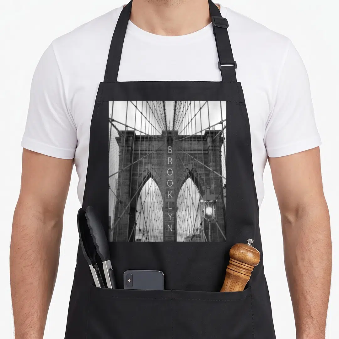 Cute bridge new york apron - Black and white photo of Brooklyn Bridge with vertical BROOKLYN text down the center stone — shown on a black cotton canvas apron against a white background