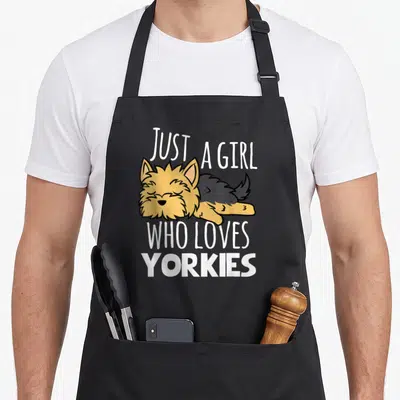Yorky yorkshire apron - Sleeping tan and grey cartoon dog surrounded by white text Just A Girl Who Loves Yorkies — shown on a black cotton canvas apron against a white background