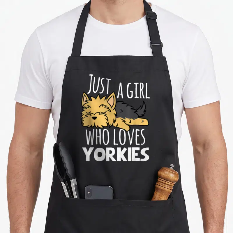 Yorky yorkshire apron - Sleeping tan and grey cartoon dog surrounded by white text Just A Girl Who Loves Yorkies — shown on a black cotton canvas apron against a white background